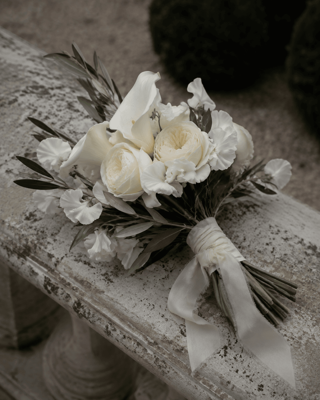 Design concept: an ivory bridal bouquet with loose ribbon on a stone bench